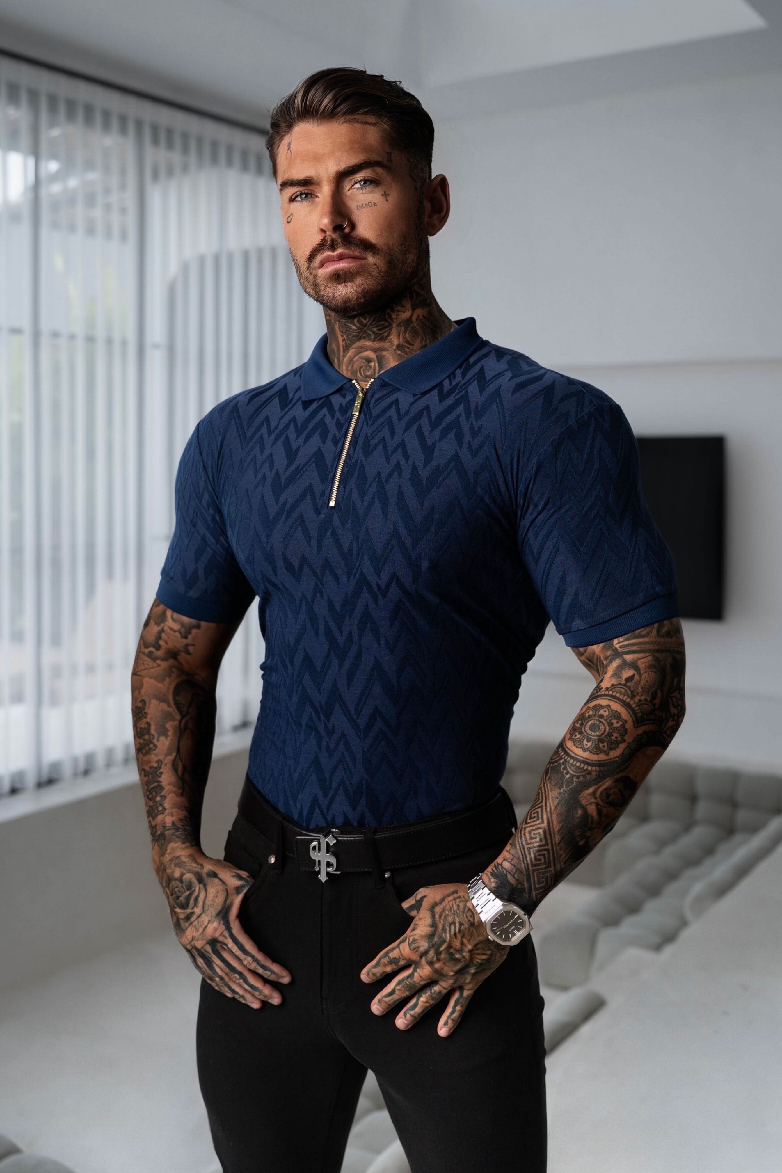 Man wearing a blue patterned shirt and black pants in a modern indoor setting