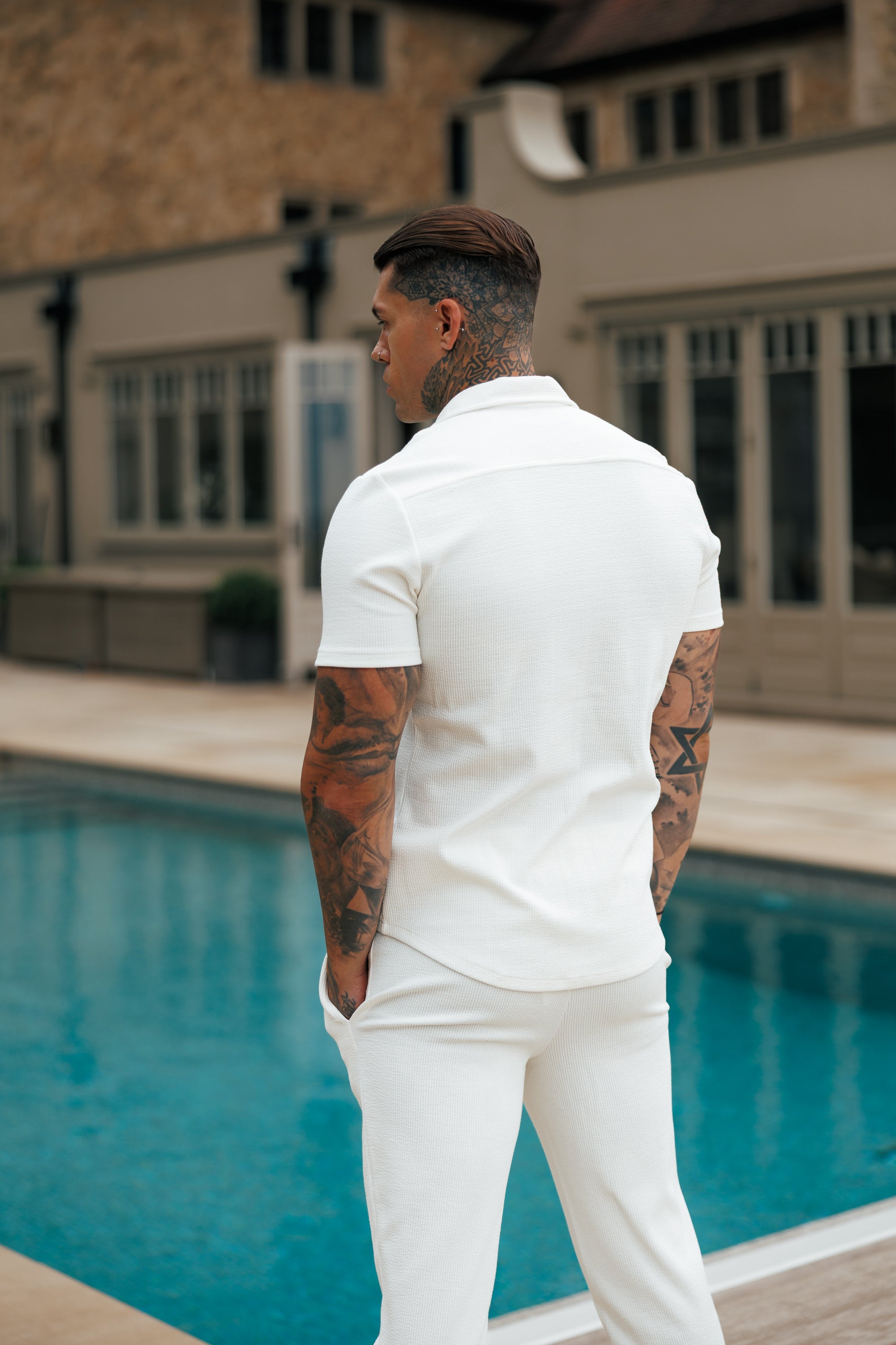 Man in a white outfit standing by a pool with a building in the background