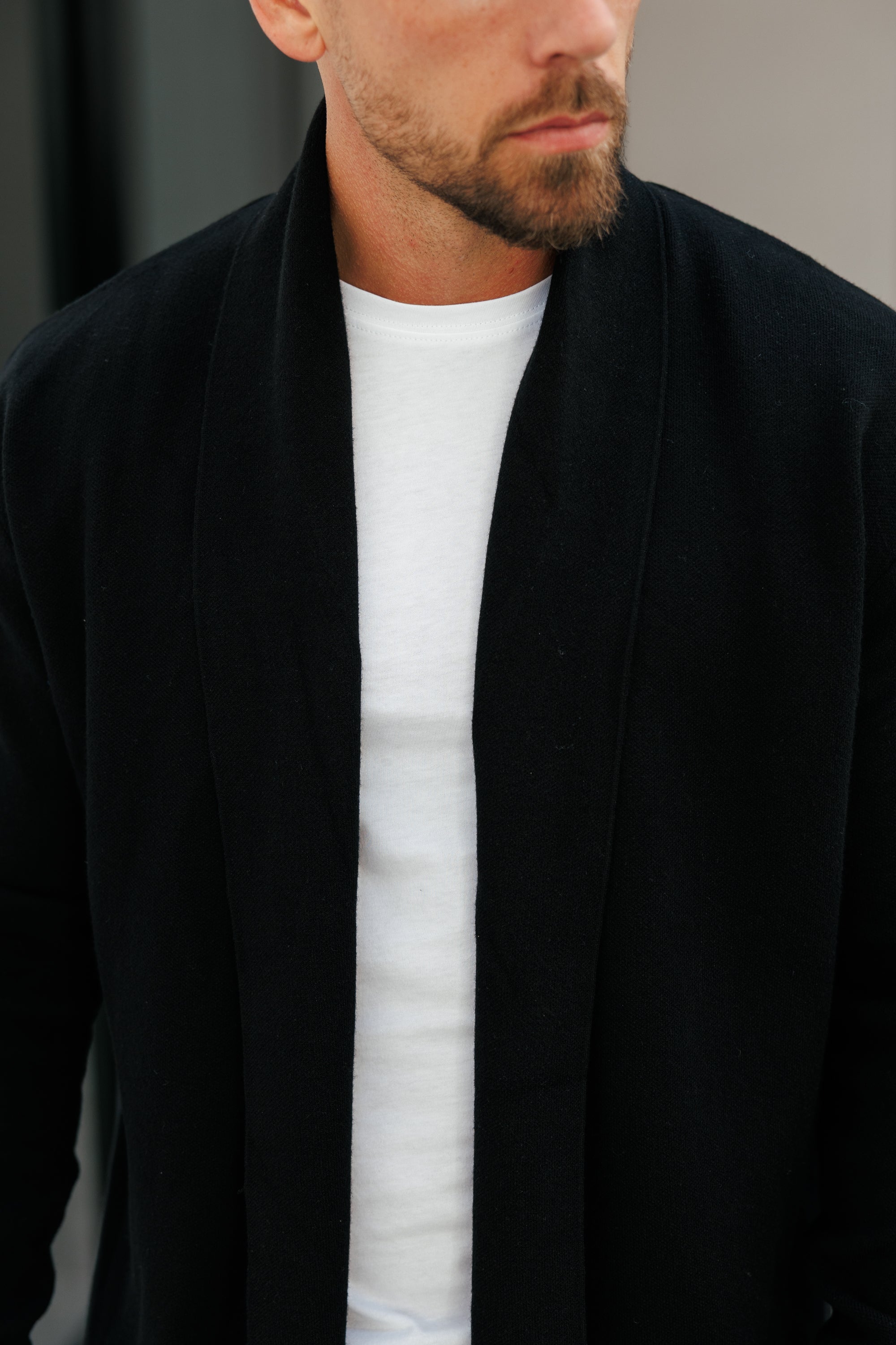 Man wearing a black coat over a white shirt against a neutral background
