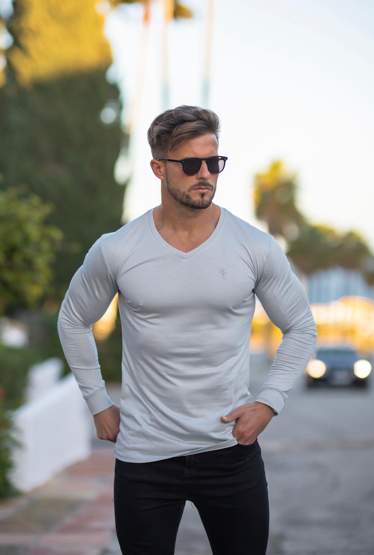 A man wearing a light grey long-sleeve V-neck crew t-shirt paired with black pants, standing on a street.